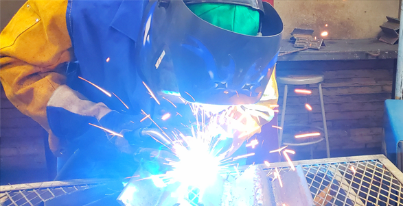 A person in a welding safety suit and face protection welds together metal objects