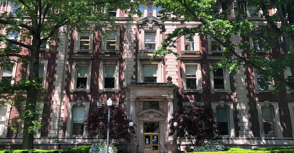 An exterior shot of Lewison Hall on a sunny day, with tall trees on both sides of the building