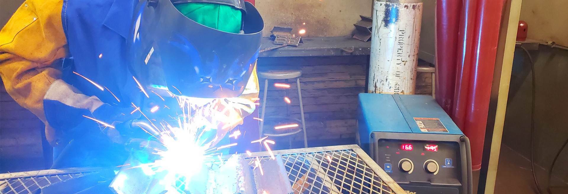 A person is welding some metal together, wearing a welding suit and helmet