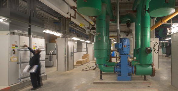 A large green and blue boiler with a man checking controls on the left side of the room