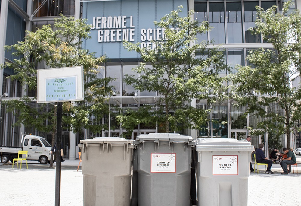 Three bins and a sign that says "Free Shredding" sit in the Small Square in front of the Jerome L. Greene Science Center