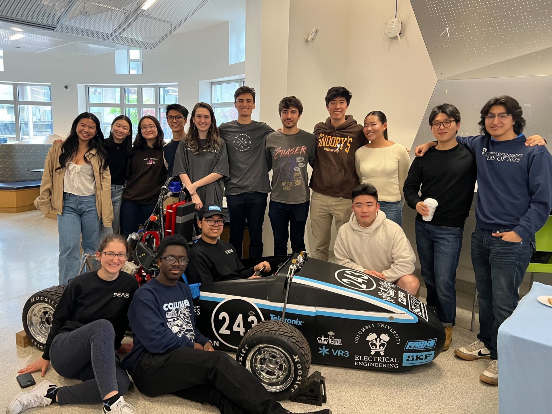 A group of students gather together in front of a mini Formula racing car.