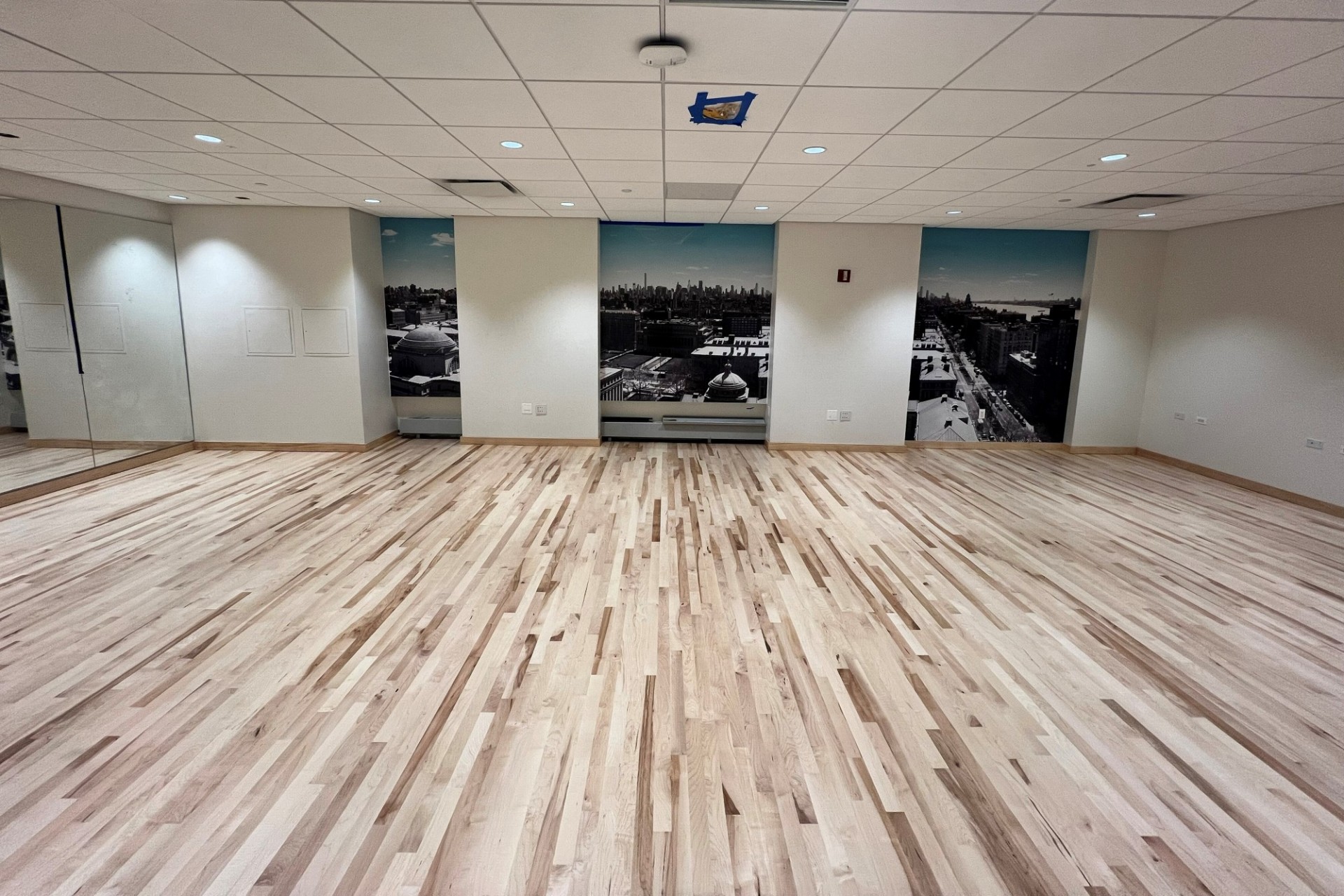 An empty room in Lerner Hall with new wooden flooring and a mirror panel wall.