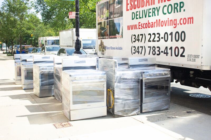 Stoves wrapped in plastic sit on the side walk next to a moving truck.