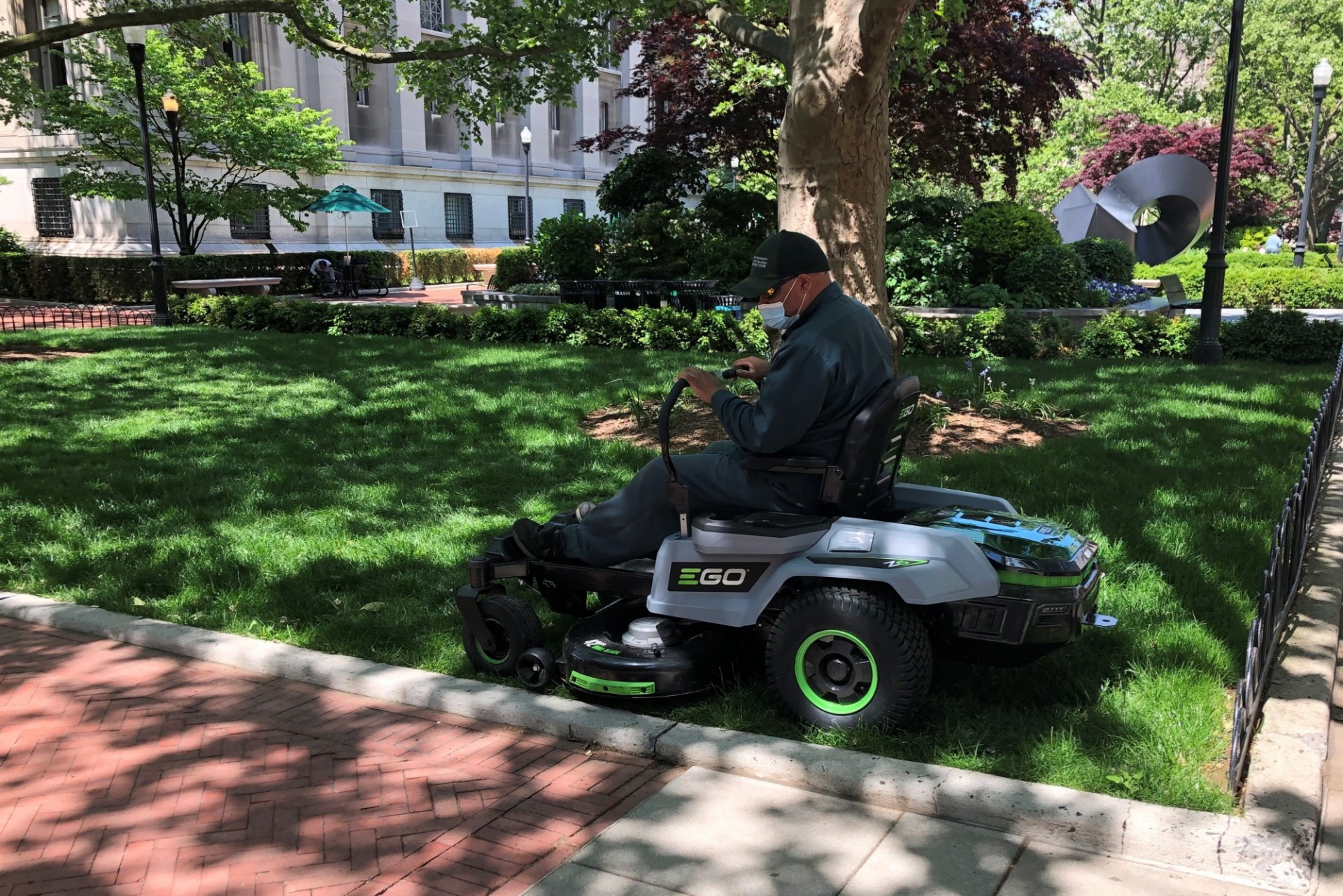A person sitting in an electrical riding lawnmower, mowing a patch of grass next to Low Library.
