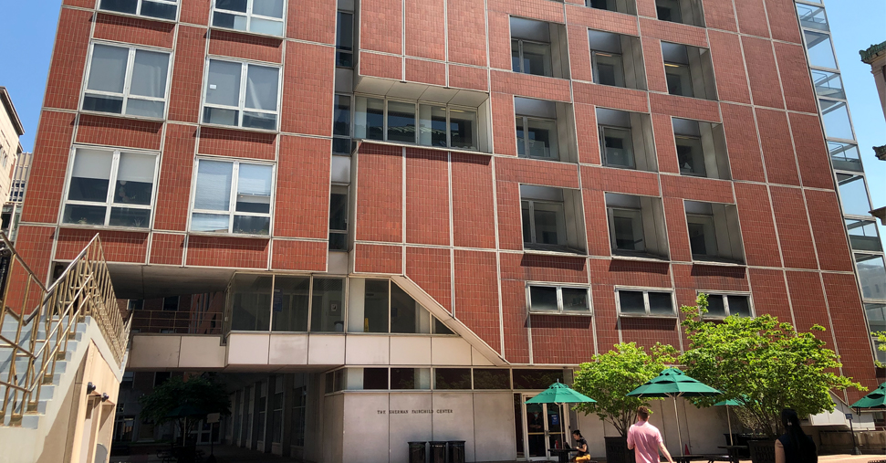 An exterior shot of the Fairchild Building on a sunny day with tented tables to the right of the entrance and a couple of small trees.