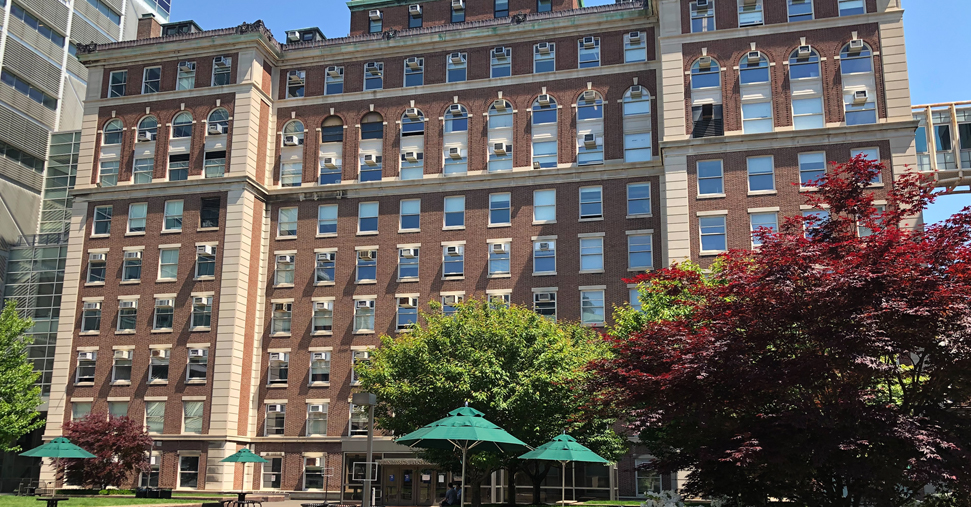A view of Pupin Hall, a Beaux Arts building, with trees and green tented tables in front of the building
