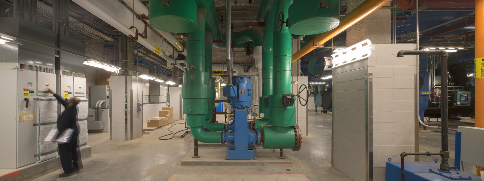 The interior of the Central Energy Plant that is full of plant equipment, with a man on the side of the room checking a panel