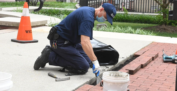 A person kneels down to install brick pavers on the pathway