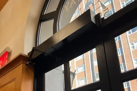 A black accessible door operator that has been installed at the top of a door.