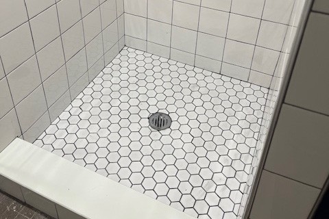 A new shower pan has been installed in showers on the 8th floor of Schapiro Hall. New white hexagon tile flooring inside of a shower.