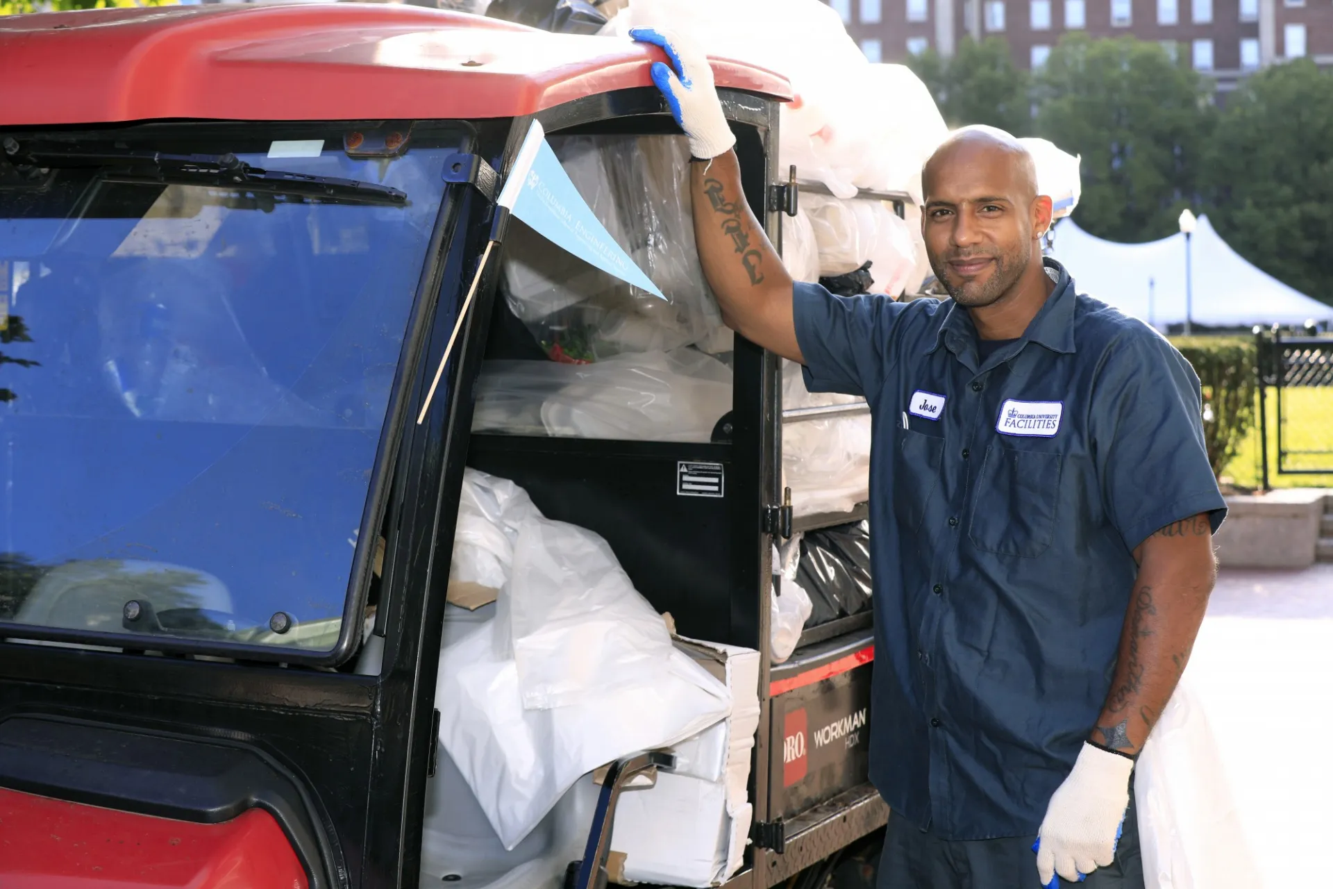 A Facilities and Operations employee stands by a mini truck that is filled with bags of recycling.